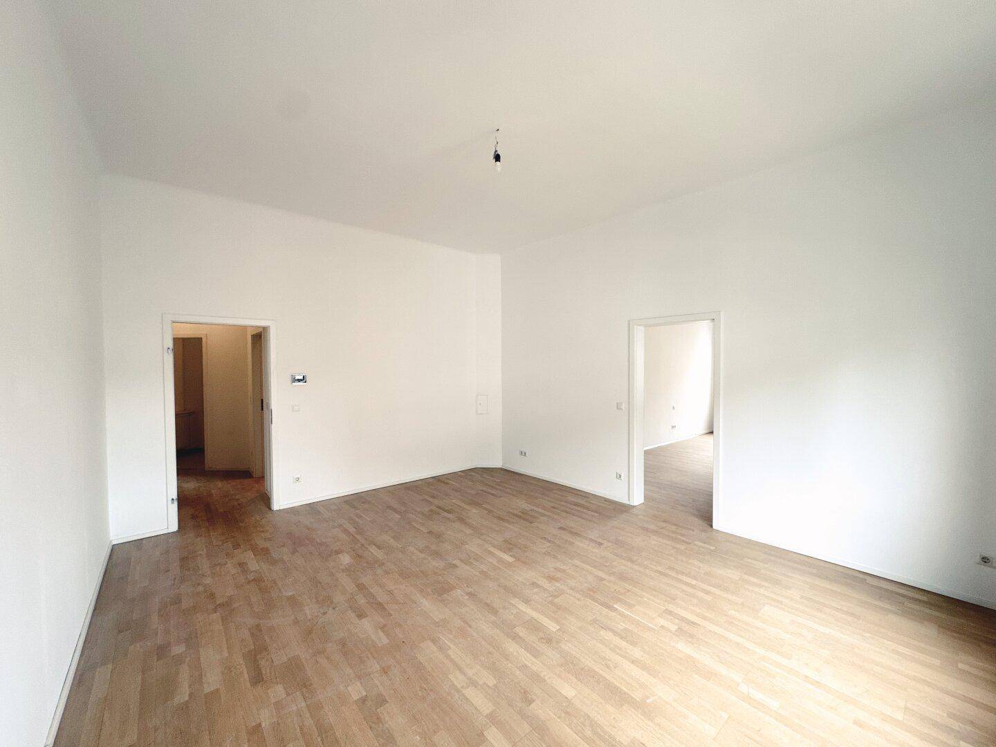 Geräumiges Zimmer mit hellem Parkettboden und zwei offenen Türen, ideal für flexible Nutzung.