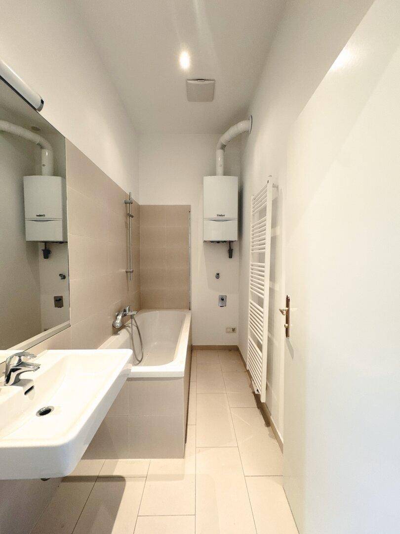 Modernes Badezimmer mit Badewanne, Waschbecken und Heizkörper, in hellen Fliesen gehalten.