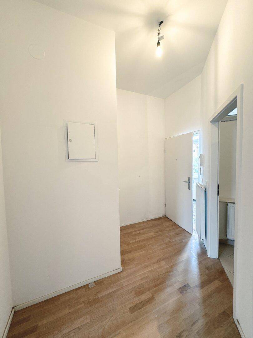 Kleiner Eingangsbereich mit Parkettboden und weiß gestrichenen Wänden, führt zur Wohnungstür.