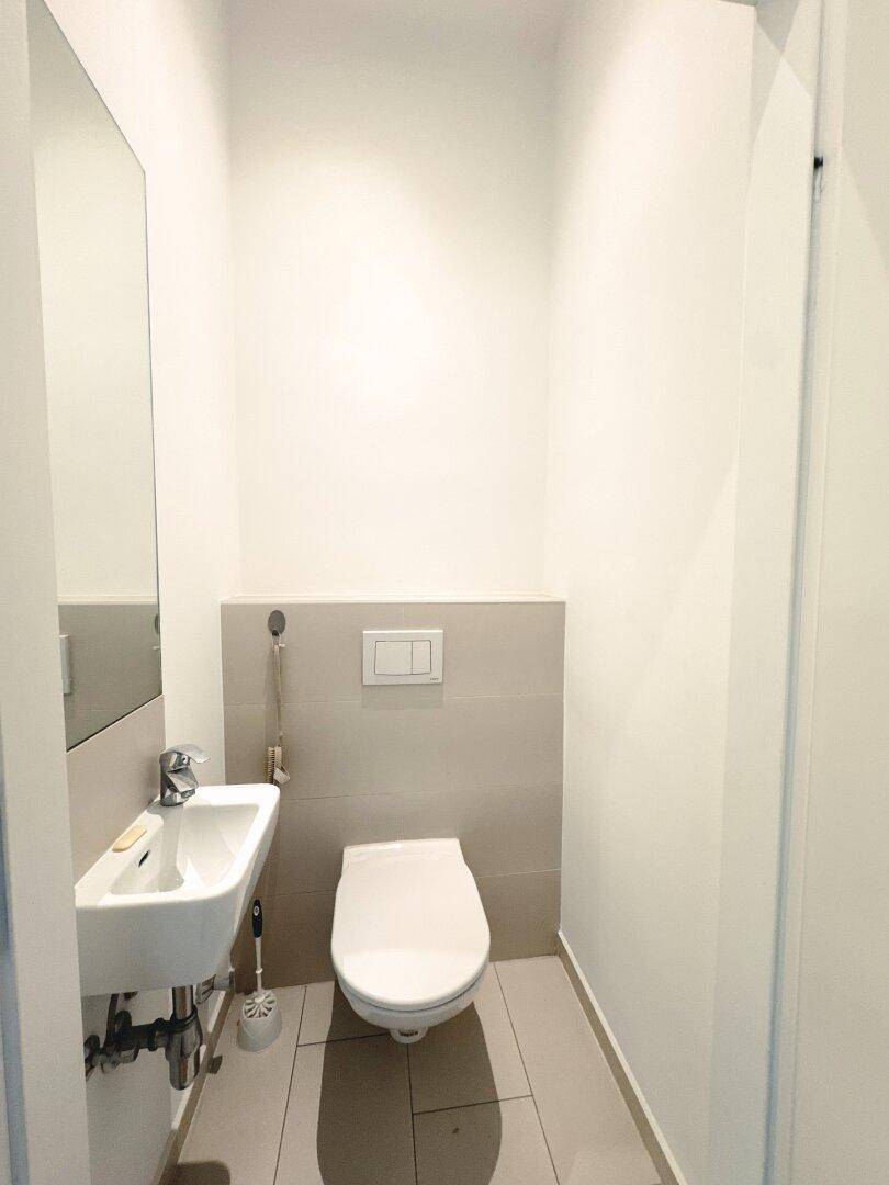 Modernes Gäste-WC mit wandhängender Toilette und kleinem Waschbecken, in hellen Fliesen.