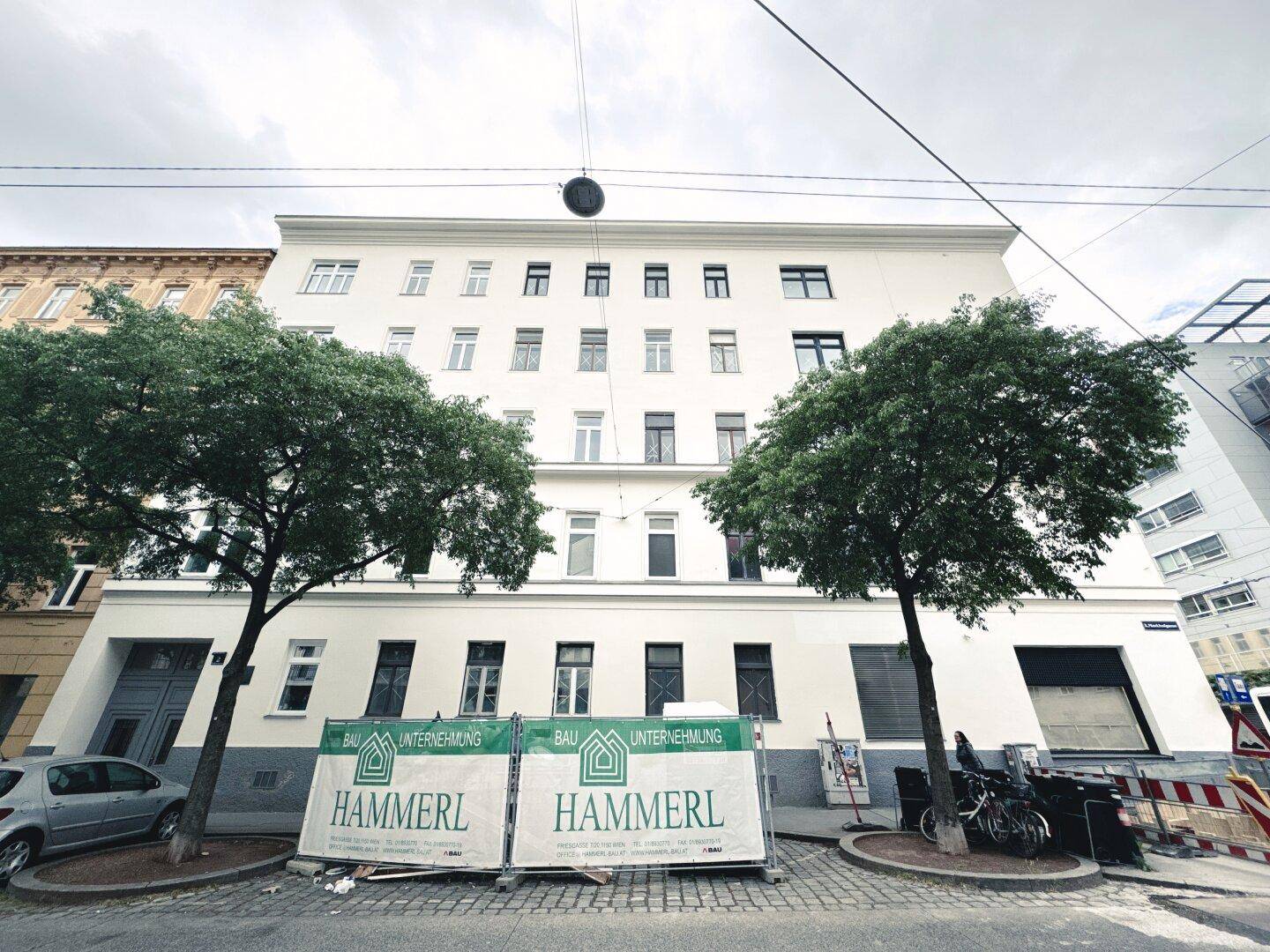 Fassade eines Mehrfamilienhauses von der Straße aus gesehen, mit Bauankündigungen.
