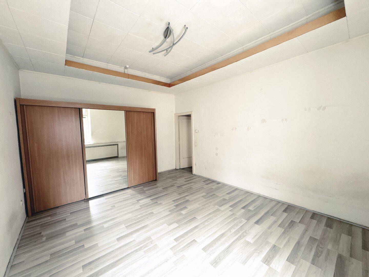Geräumiges Zimmer mit Laminatboden und einem großen Spiegelschrank.