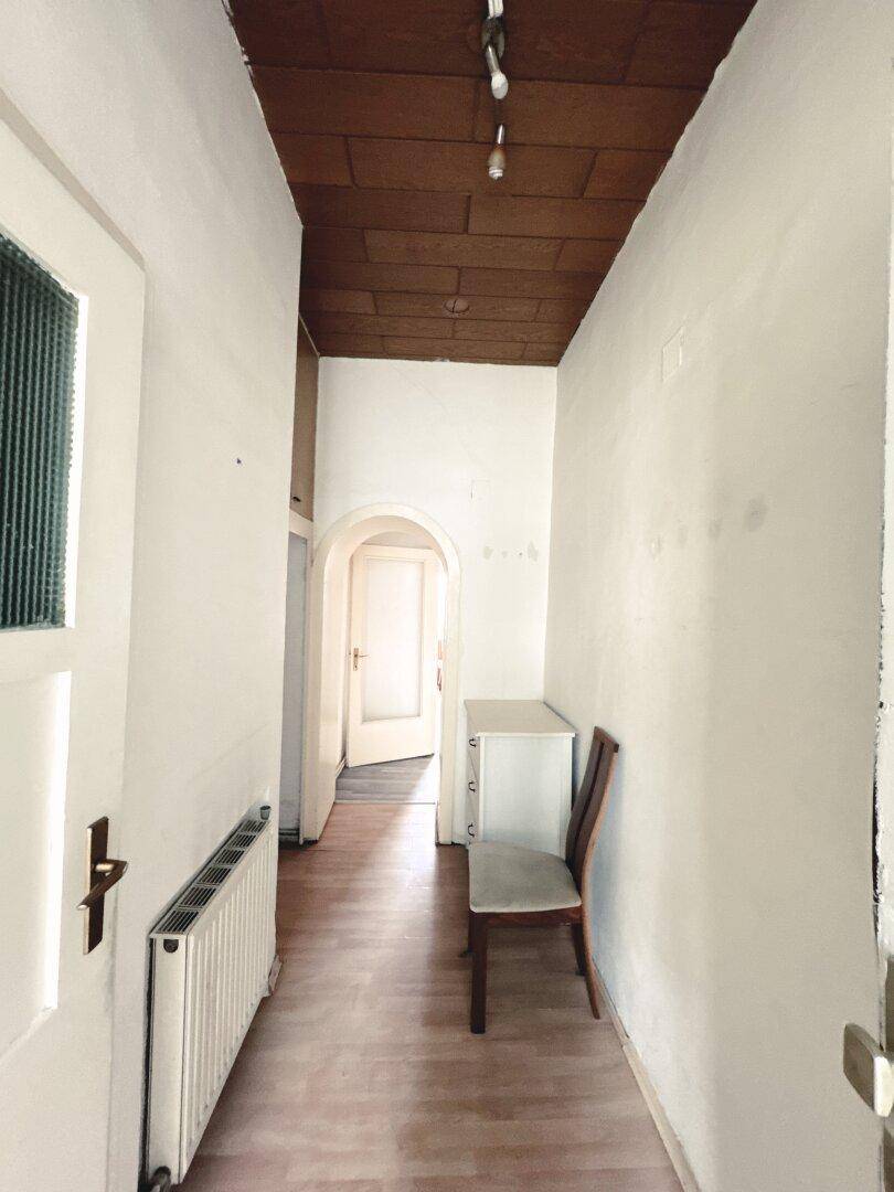 Schmaler Flur mit Holzdecke und Laminatboden, der zu weiteren Räumen führt.