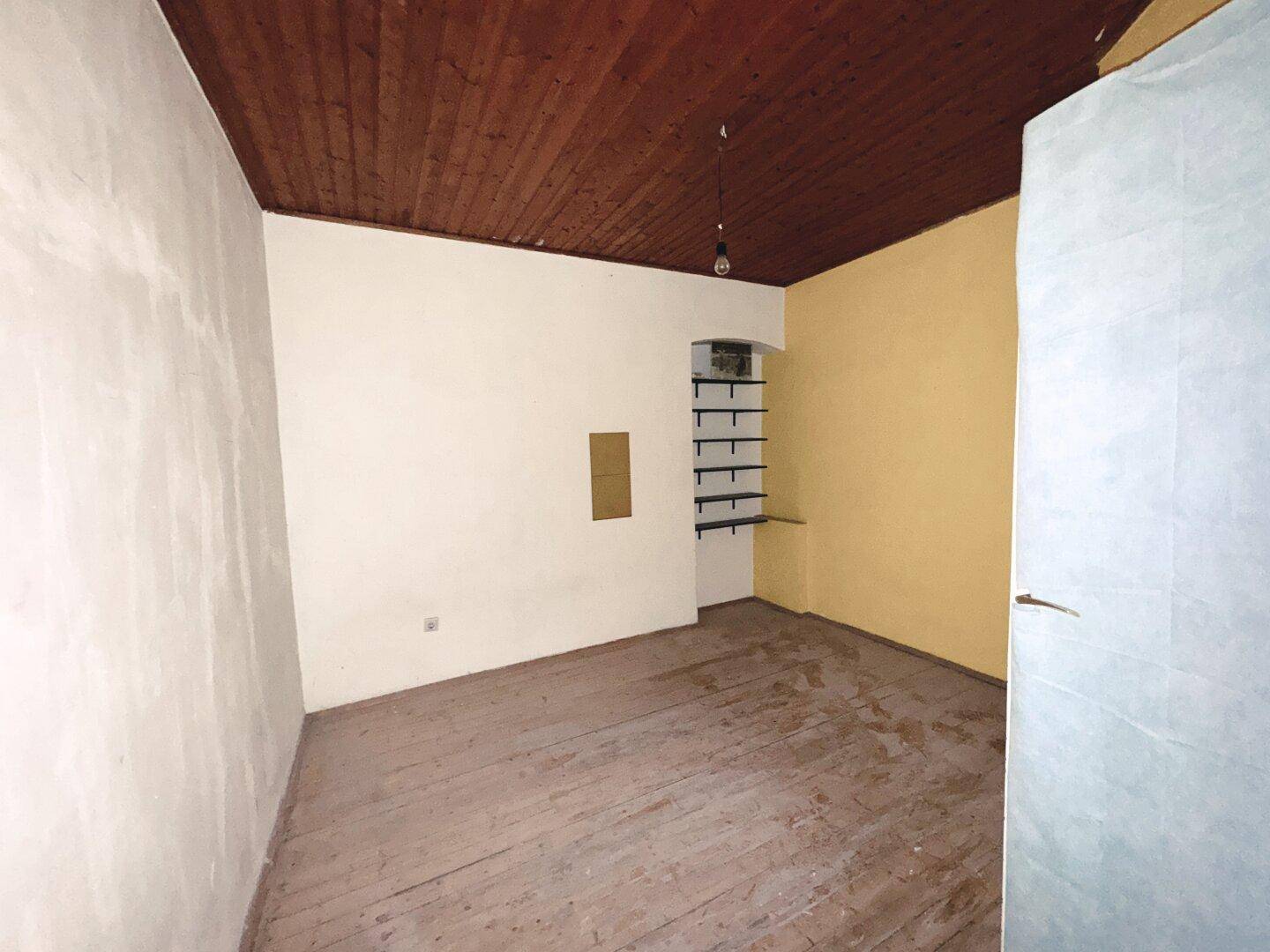 Einfaches Zimmer mit Holzdielenboden, gelber Wand und dunkler Holzdecke, ideal für Renovierung.