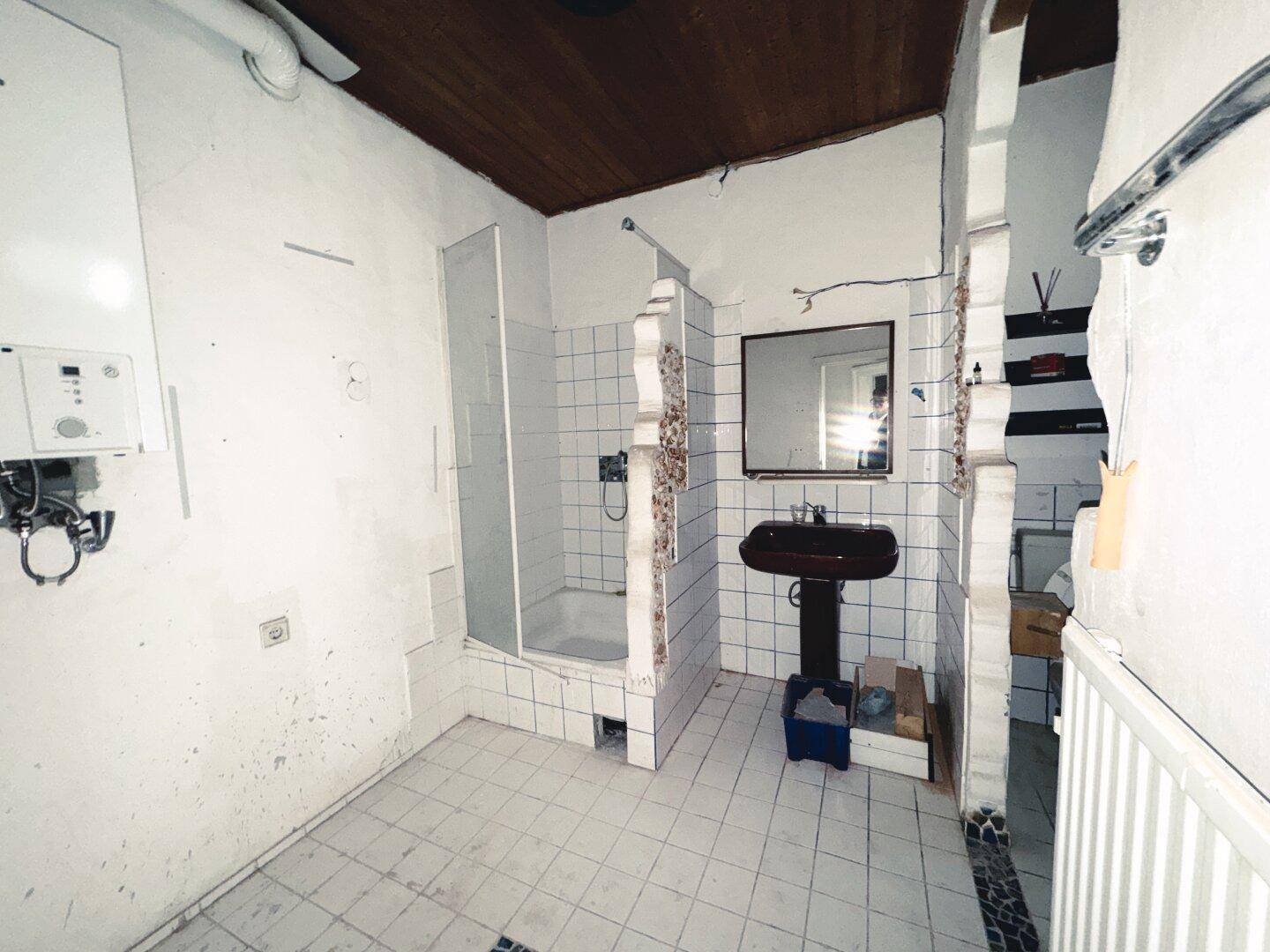 Badezimmer mit Duschkabine, Waschbecken und Gastherme, benötigt eine Modernisierung.