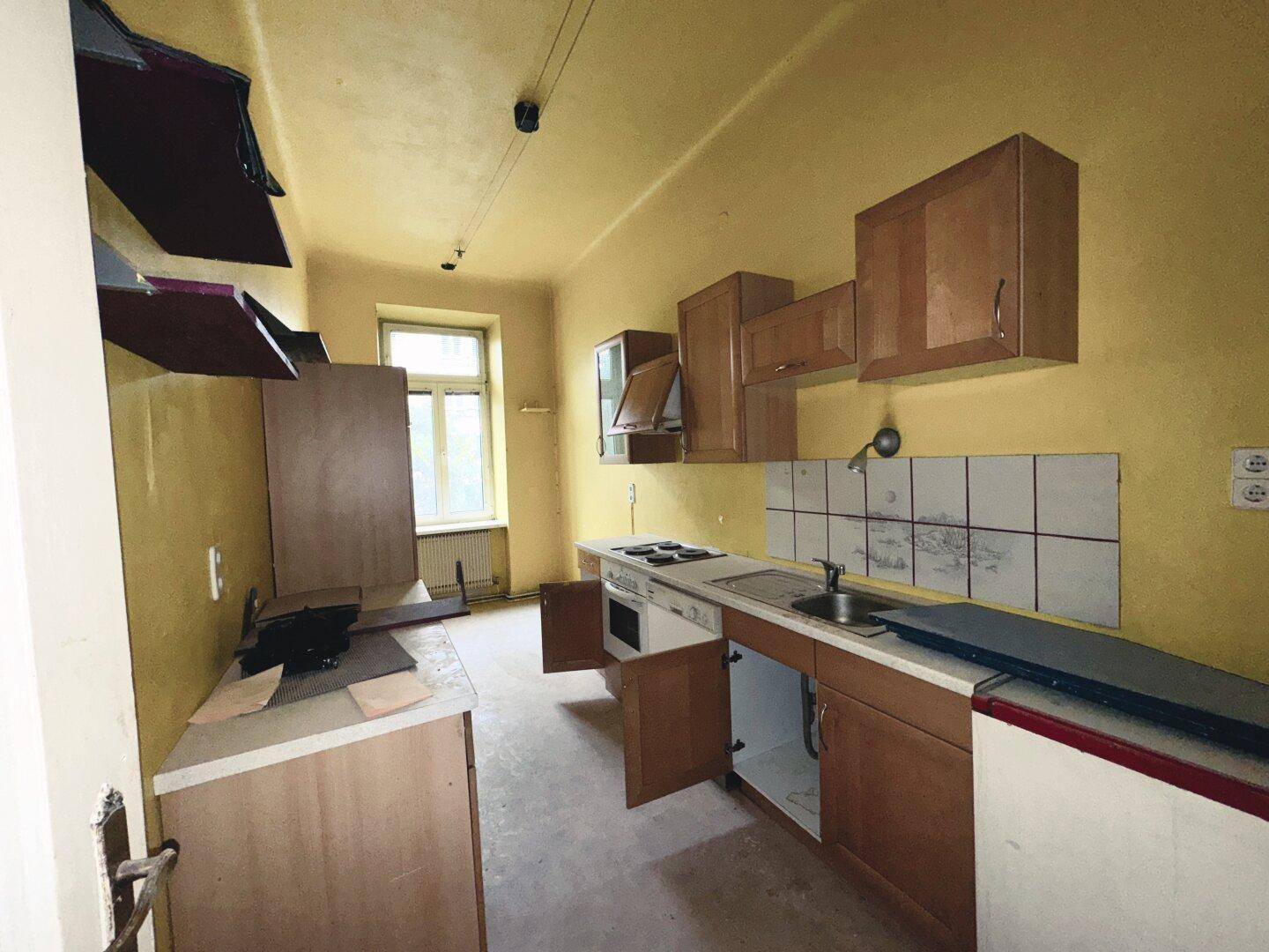 Renovierungsbedürftige Küche mit gelben Wänden, einfachen Holzschränken und altem Fliesenspiegel.
