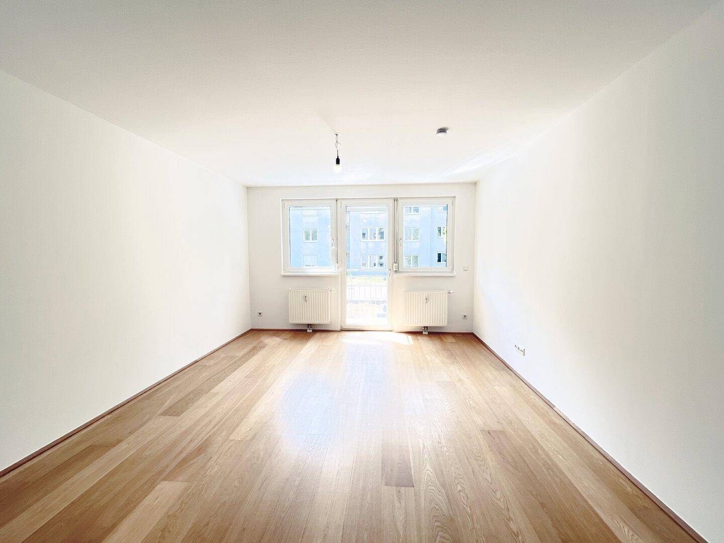 Geräumiges, helles Zimmer mit Holzboden und großen Fenstern, die den Raum lichtdurchfluten.