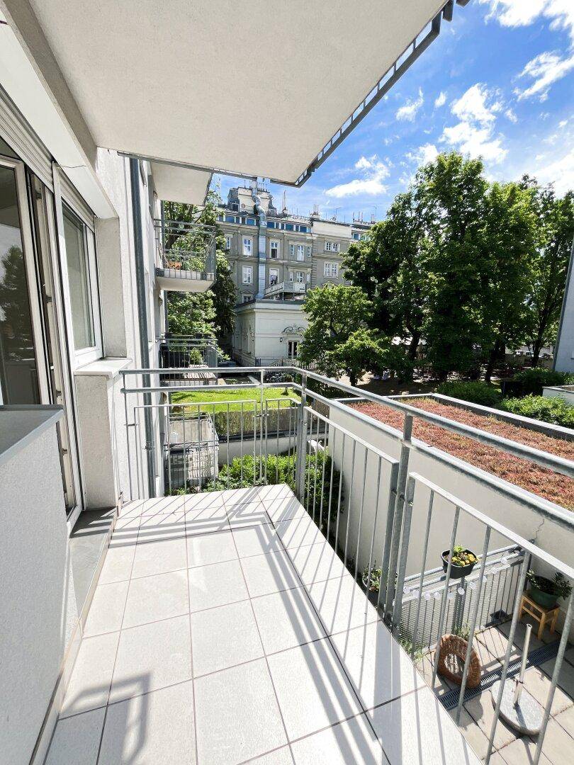 Sonniger Balkon mit Fliesen und Metallgeländer, bietet einen Ausblick ins Grüne.
