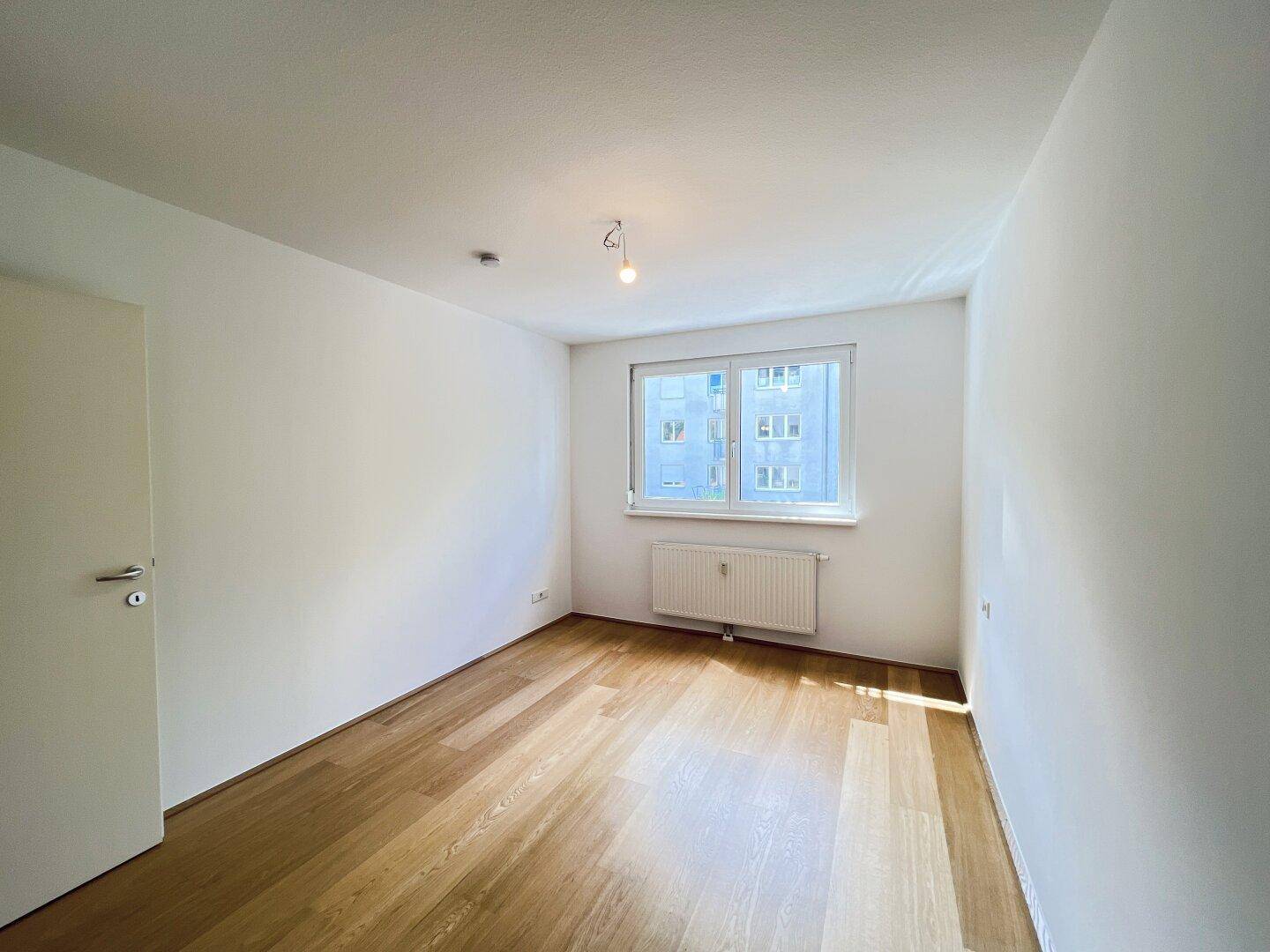 Geräumiges Zimmer mit Holzboden und großem Fenster, ideal als Schlafzimmer.