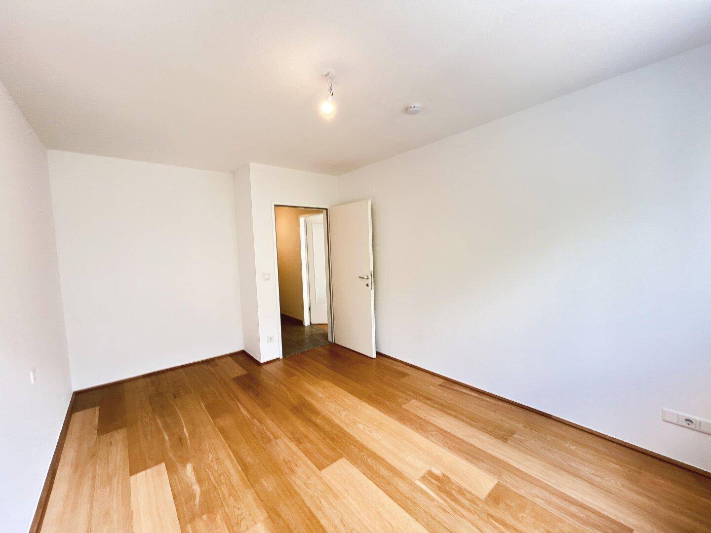 Leeres Zimmer mit Parkettboden und Zugang zu einem gefliesten Flur.