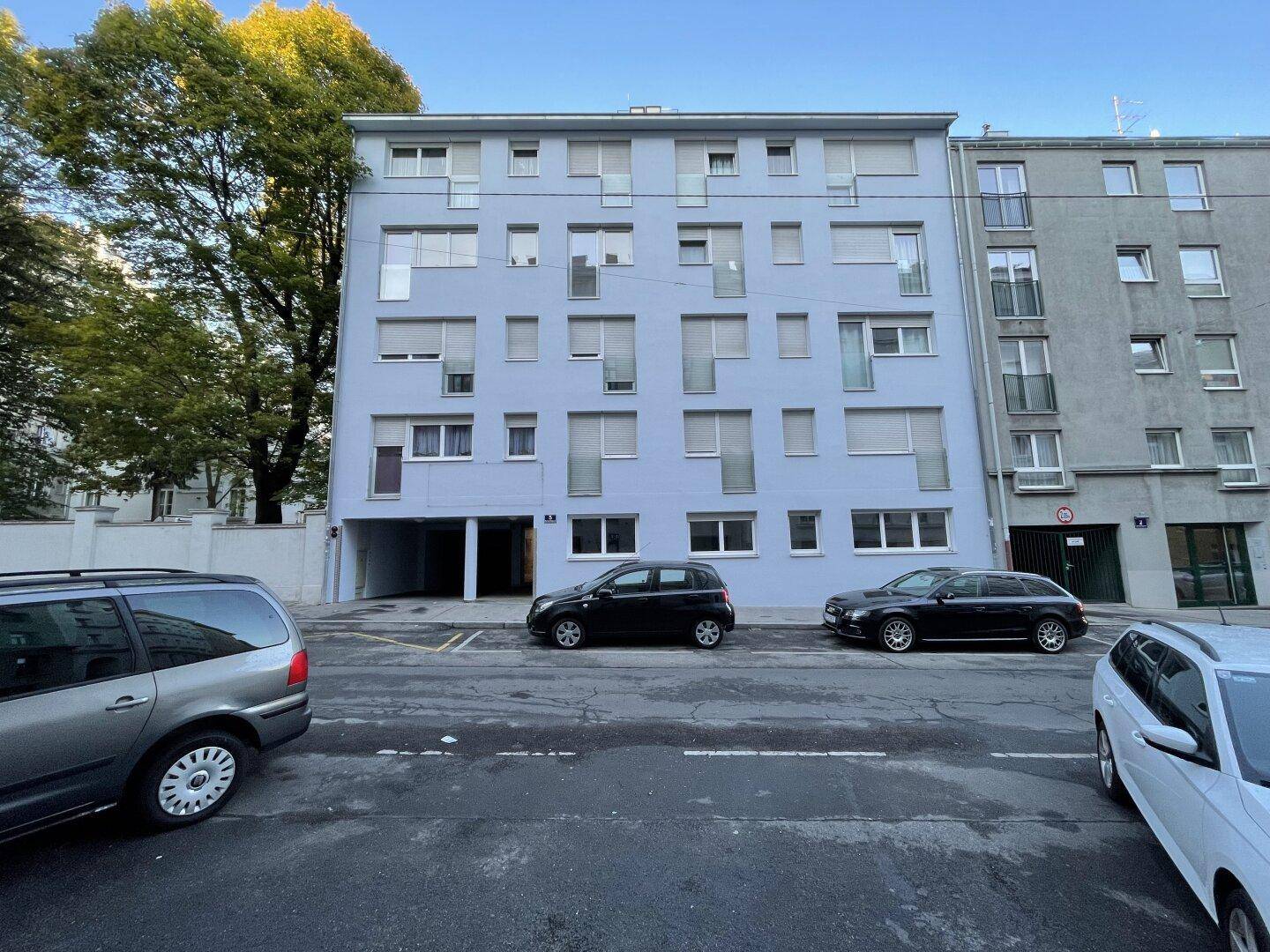 Moderne Fassade eines Mehrfamilienhauses mit vielen Fenstern und Parkplätzen davor.