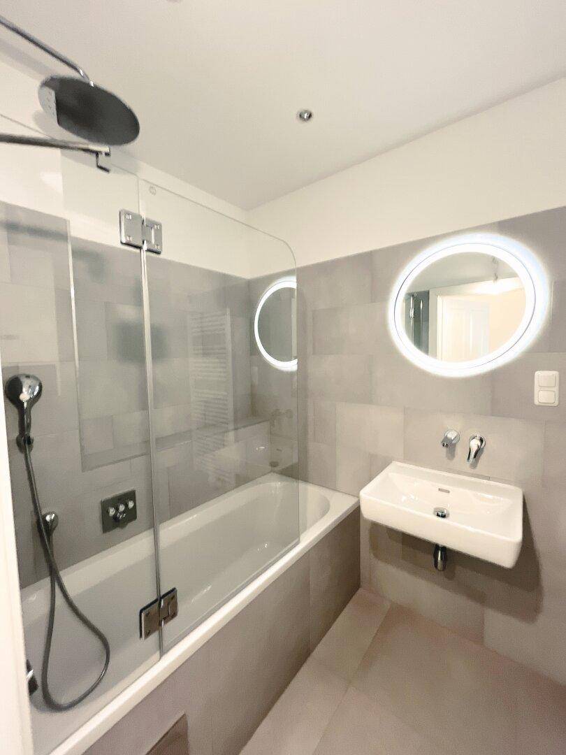 Modernes Badezimmer mit Badewanne, Duschfunktion und beleuchtetem Spiegel.