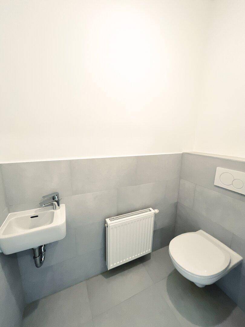 Separates Gäste-WC mit Wand-WC, kleinem Waschbecken und Heizkörper.
