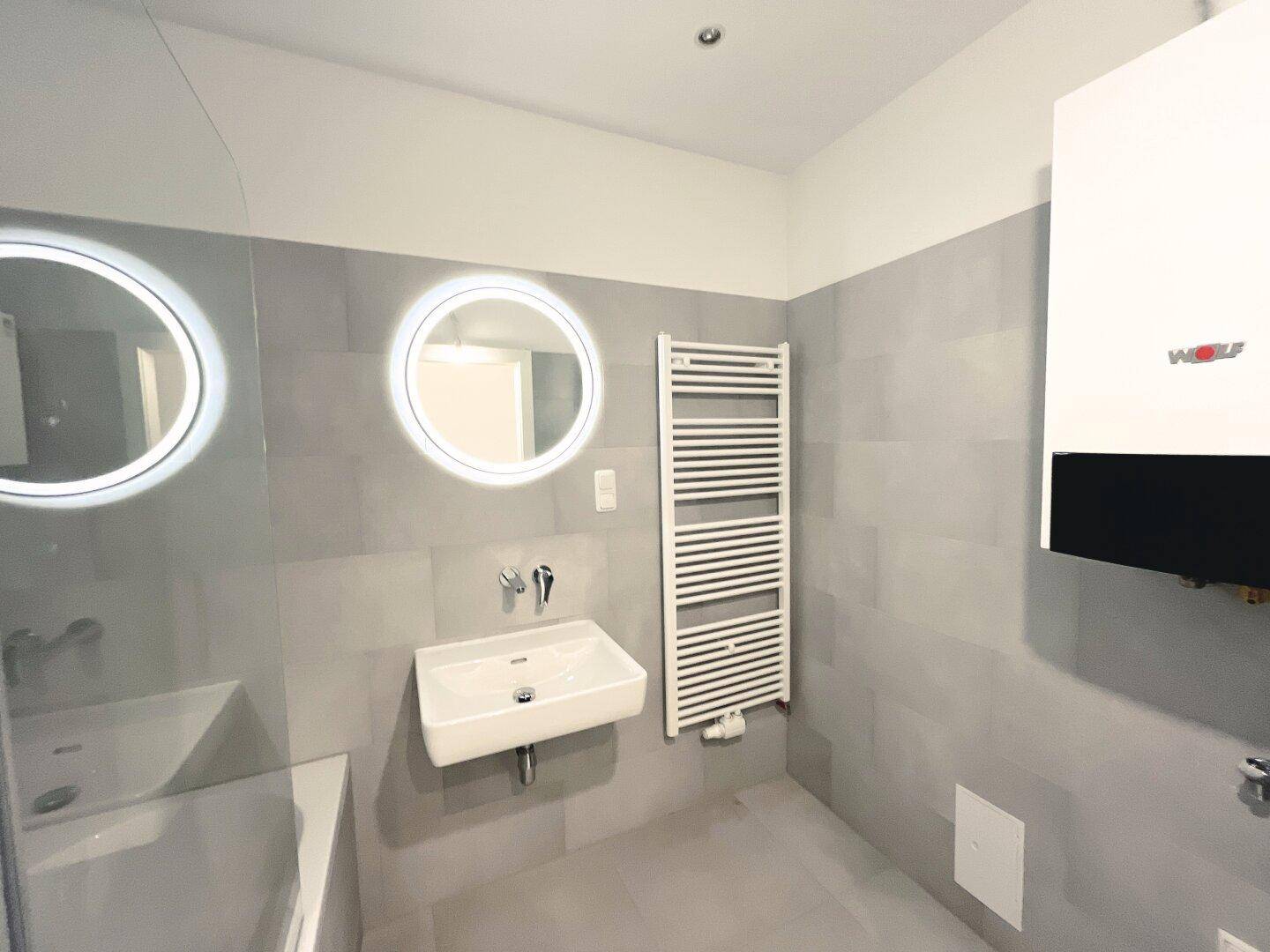 Helles Badezimmer mit modernem Waschbecken, beleuchtetem Spiegel und Handtuchheizkörper.