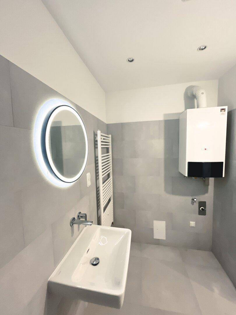 Modernes Badezimmer mit Waschbecken, beleuchtetem Spiegel und Heiztherme.
