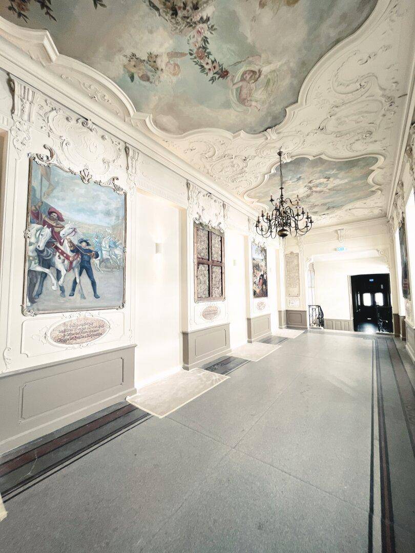 Prunkvoller Flur mit historischen Wandgemälden, Stuckdecken und Kronleuchter.