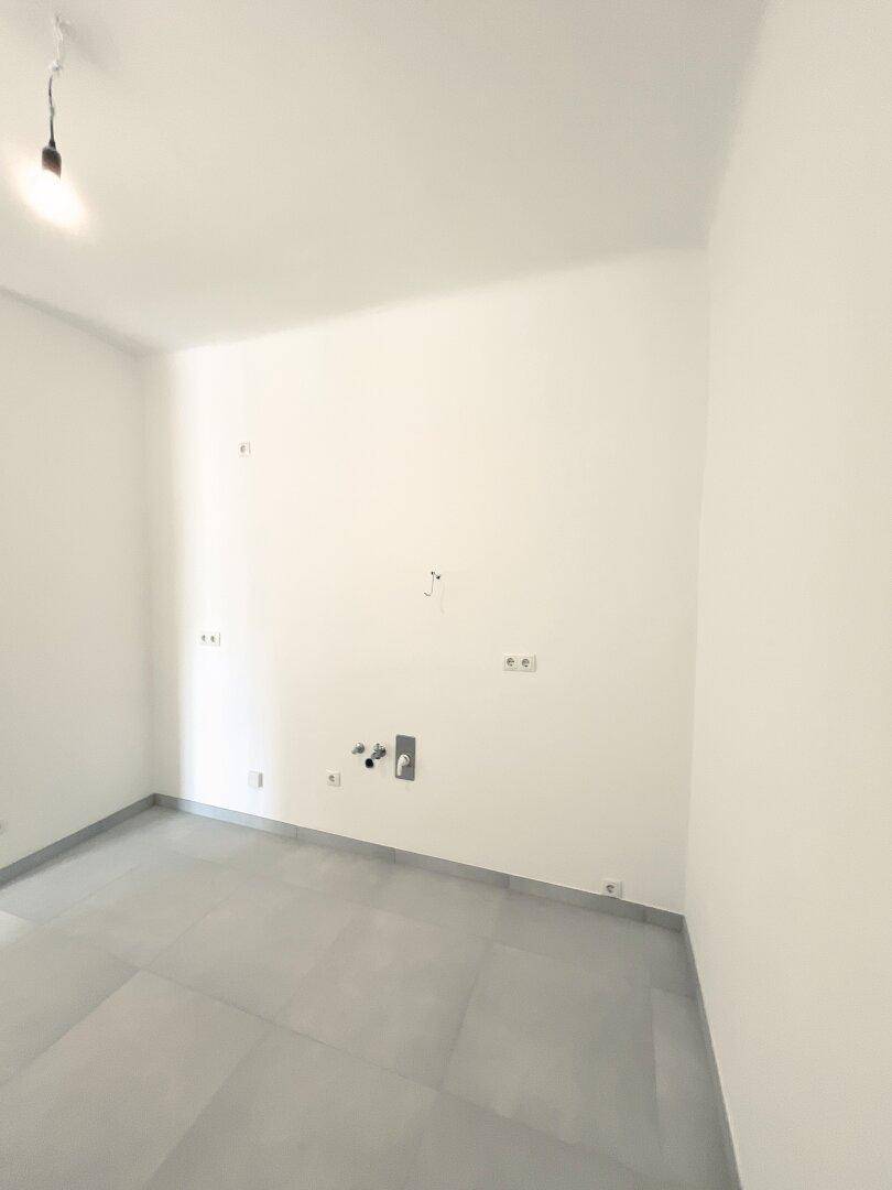 Leerer Raum mit Fliesenboden und Anschlüssen für eine zukünftige Küche.