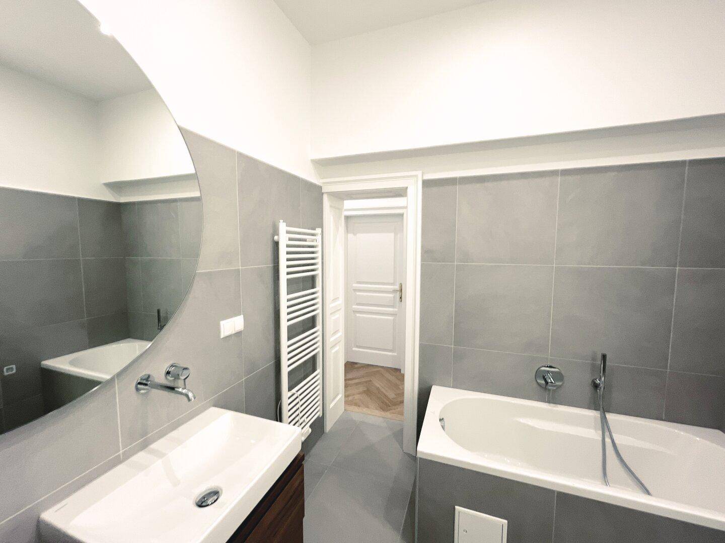 Modernes Badezimmer mit Badewanne, Einzelwaschbecken und beheiztem Handtuchhalter.