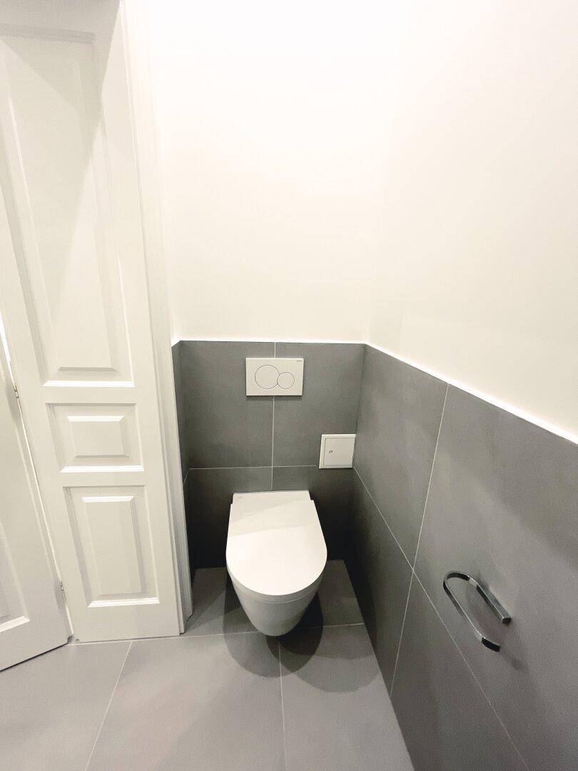 Schlichtes Gäste-WC mit grauen Fliesen und wandhängendem WC, ideal für Besucher.