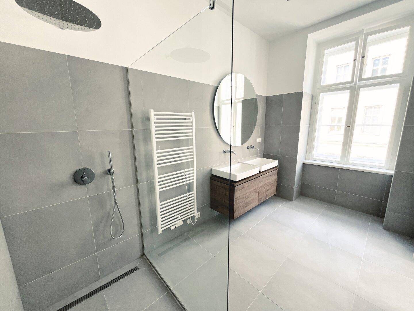 Helles Badezimmer mit großer Dusche, Doppelwaschbecken und Fenster für natürliche Belüftung.