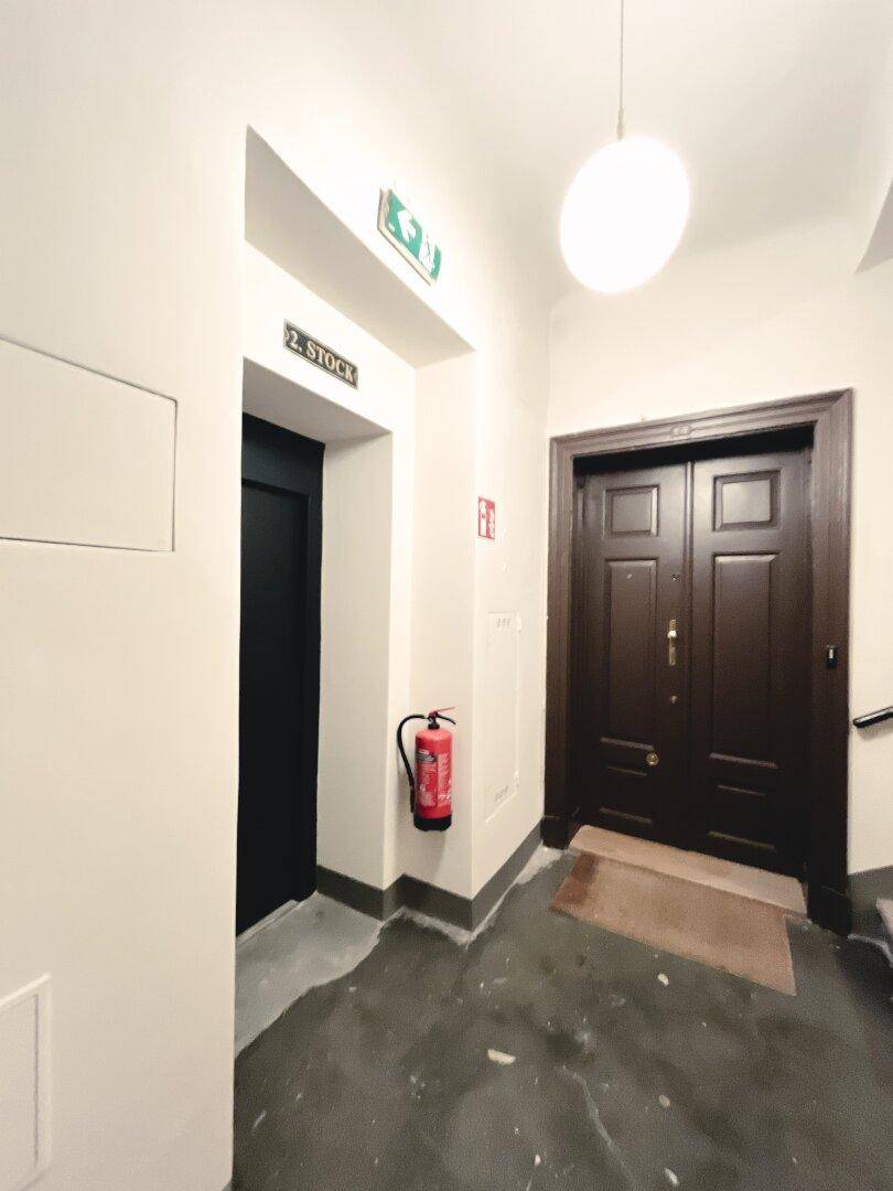 Heller Hausflur mit Aufzug und einer dunklen Eingangstür zur Wohnung im zweiten Stock.