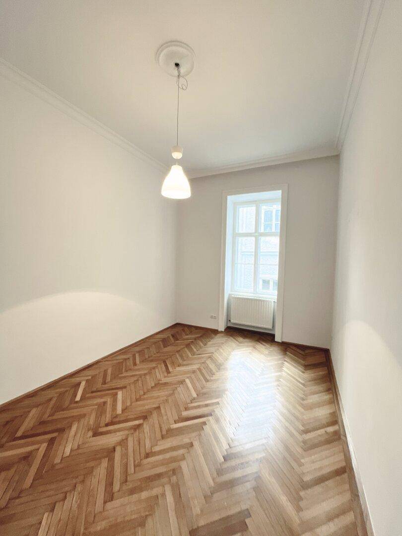 Geräumiges Zimmer mit klassischem Fischgrätparkett und Stuckverzierung an der Decke.