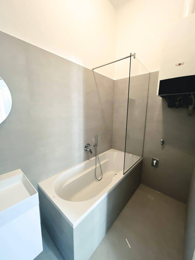 Modernes Badezimmer mit Badewanne, Duschabtrennung und grauen Fliesen.