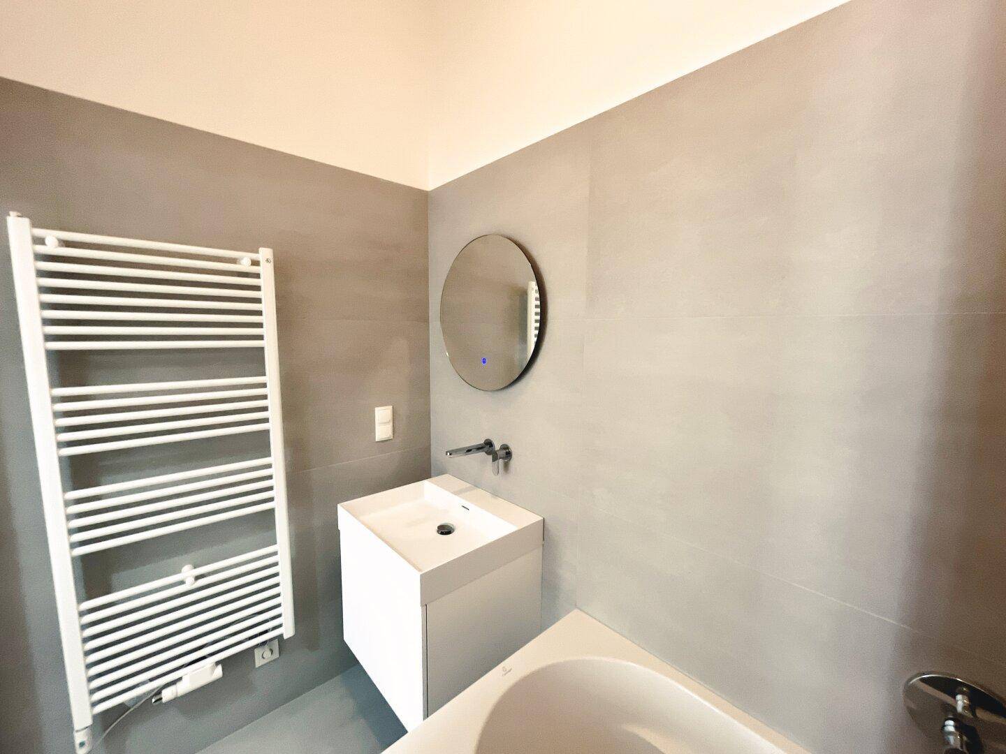Badezimmer mit modernem Waschtisch, beleuchtetem Spiegel und Handtuchheizkörper.