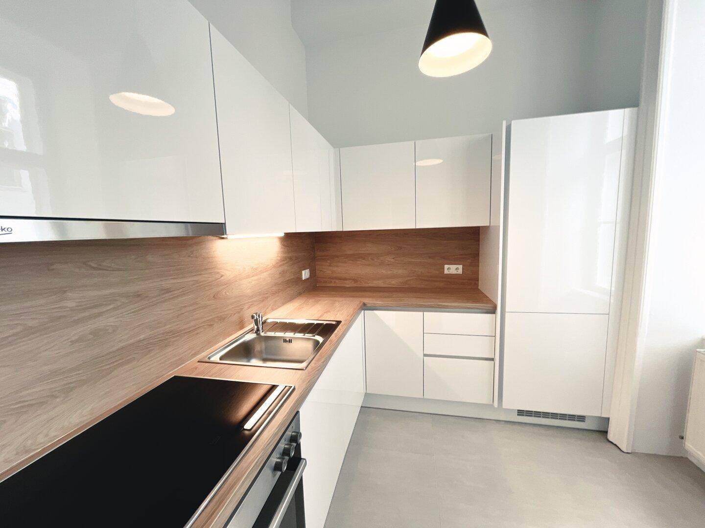 Neue Küche mit glänzenden weißen Schränken, integrierten Geräten und Holzdetails.
