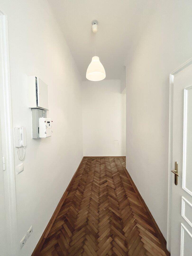 Heller Flur mit klassischem Fischgrätparkett und Gegensprechanlage an der Wand.