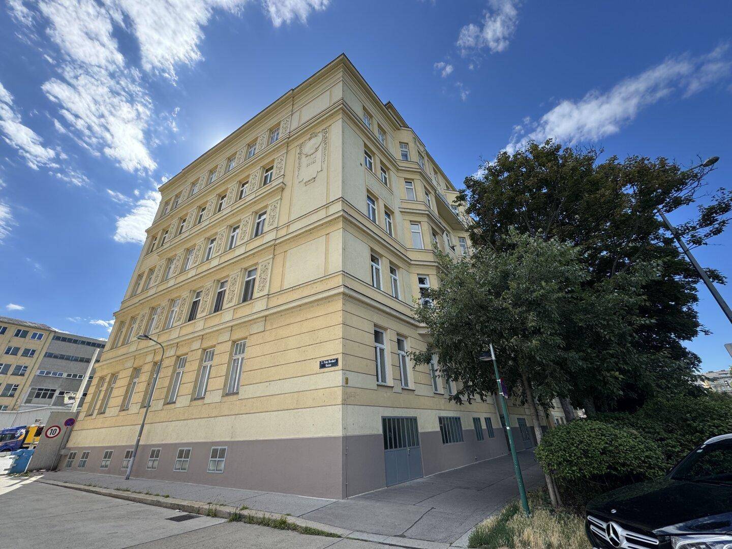 Klassisches Gebäude mit gelber Fassade, vielen Fenstern und einem blauen Himmel.