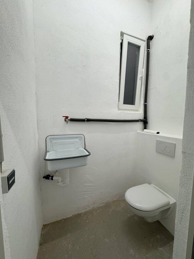 Kleine Gästetoilette mit wandhängendem WC, kleinem Waschbecken und einem Fenster.