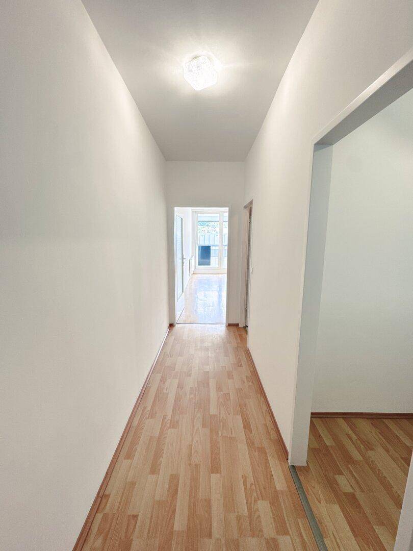 Langer, heller Flur mit Laminatboden, der zu weiteren Räumen im Apartment führt.