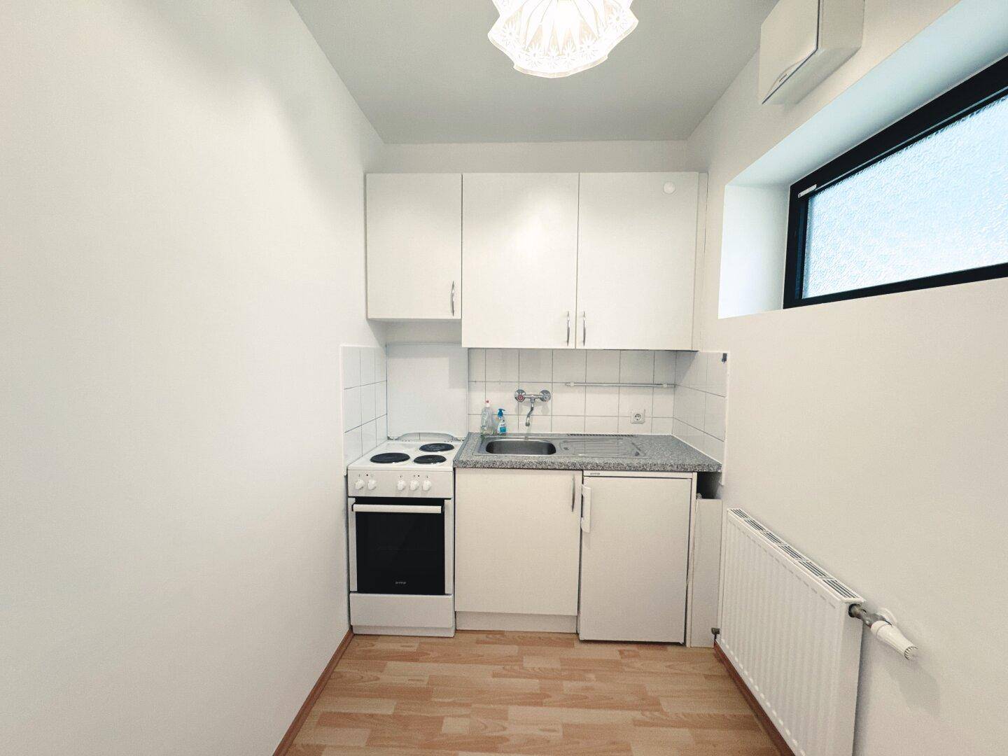 Kleine Küchenzeile mit weißen Schränken, Herd und Kühlschrank, ideal für eine Einzelperson.