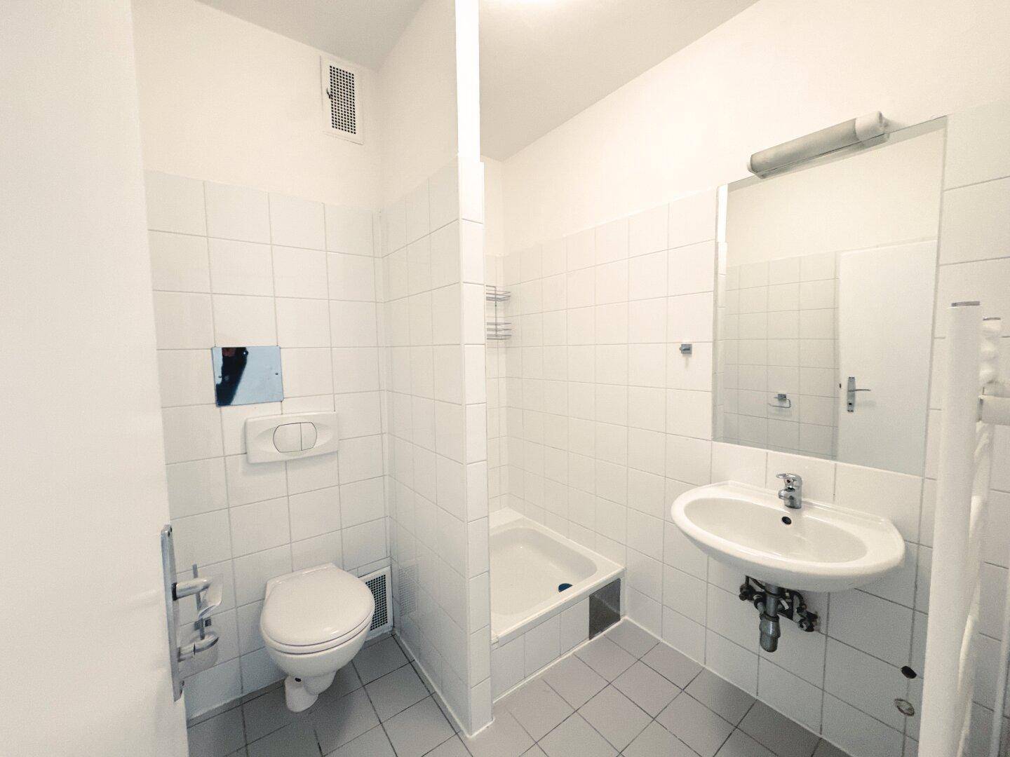Funktionales Badezimmer mit weißen Fliesen, WC, Waschbecken und einem Duschbereich.