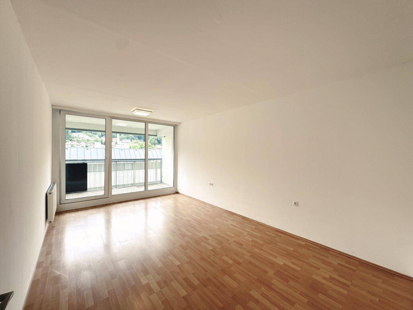 Helles Wohnzimmer mit Parkettboden und großen Fenstern, die Zugang zum Balkon bieten.