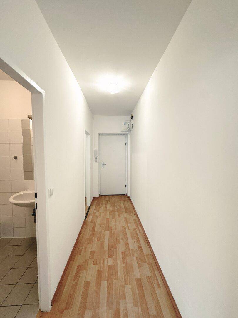 Schmaler Flur mit Laminatboden und Zugang zu einem Badezimmer auf der linken Seite.
