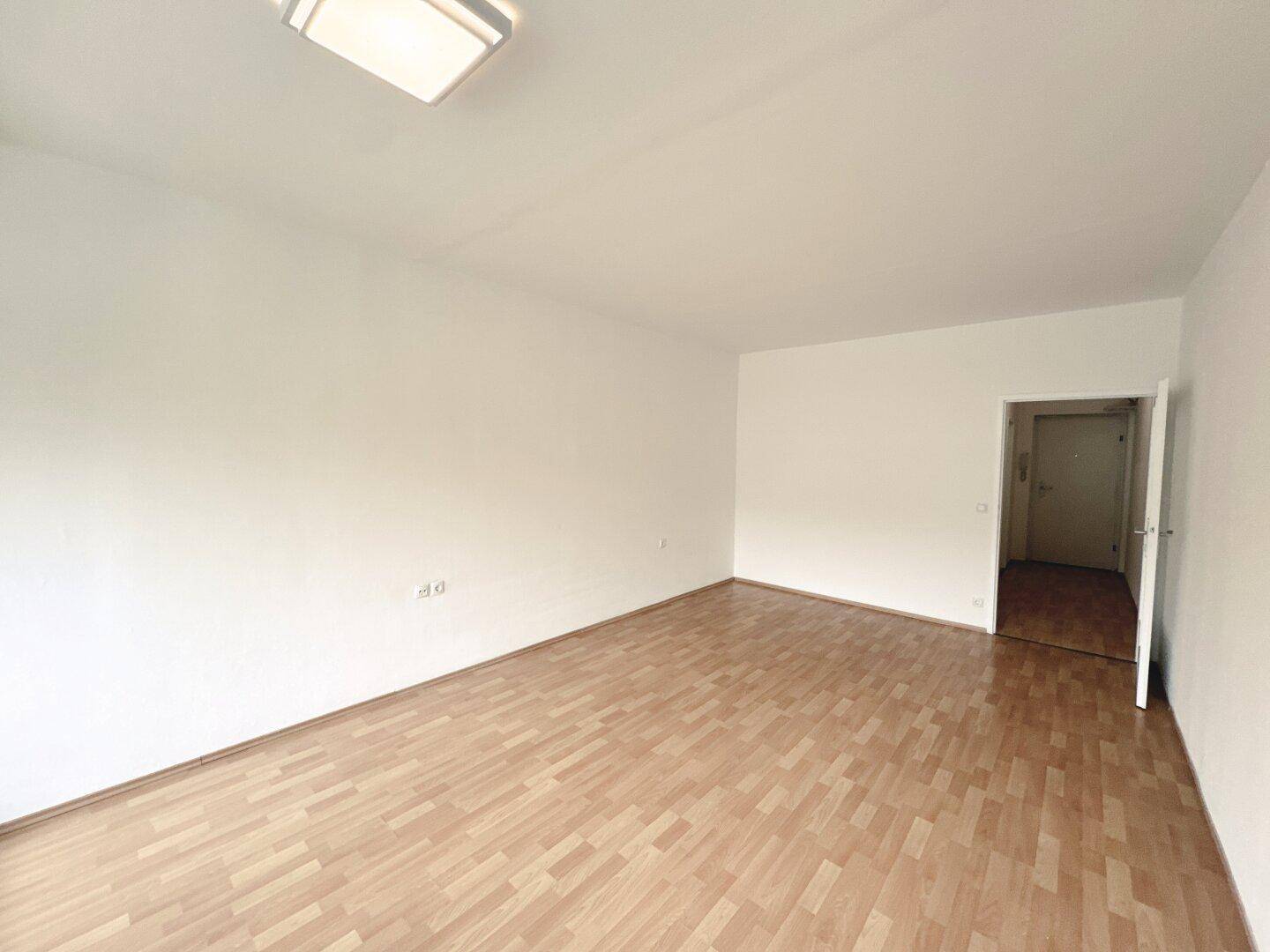 Leeres Wohnzimmer mit hellem Parkettboden und weiß gestrichenen Wänden, bereit zur Einrichtung.