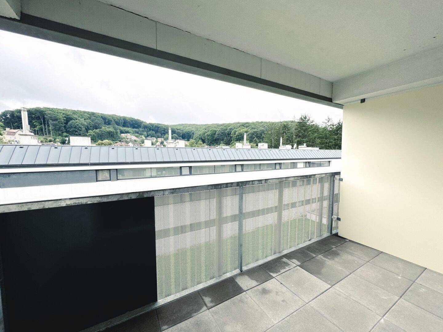 Balkon mit Fliesenboden und weitem Blick über die umliegende Landschaft und andere Gebäude.