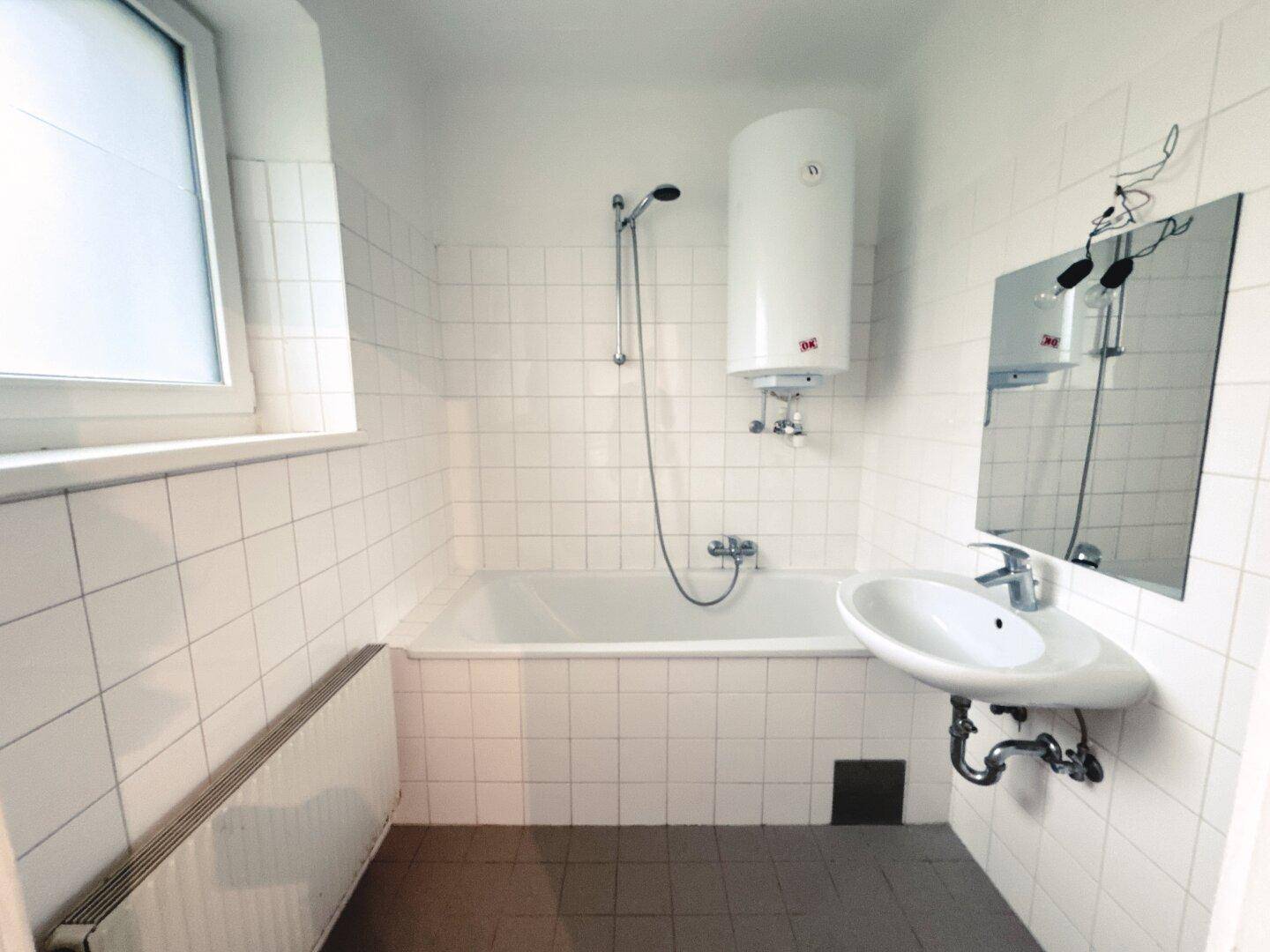Badezimmer mit Badewanne, Waschbecken, Boiler und Fenster, komplett gefliest.