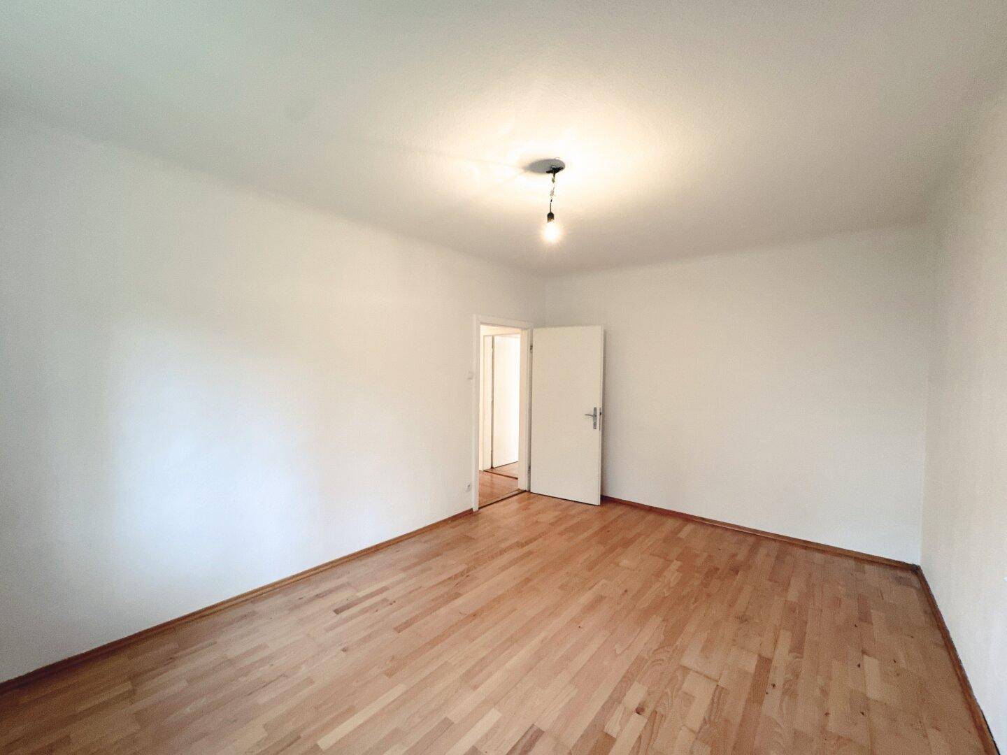 Leeres Zimmer mit Parkettboden und weiß gestrichenen Wänden, bereit zur Einrichtung.