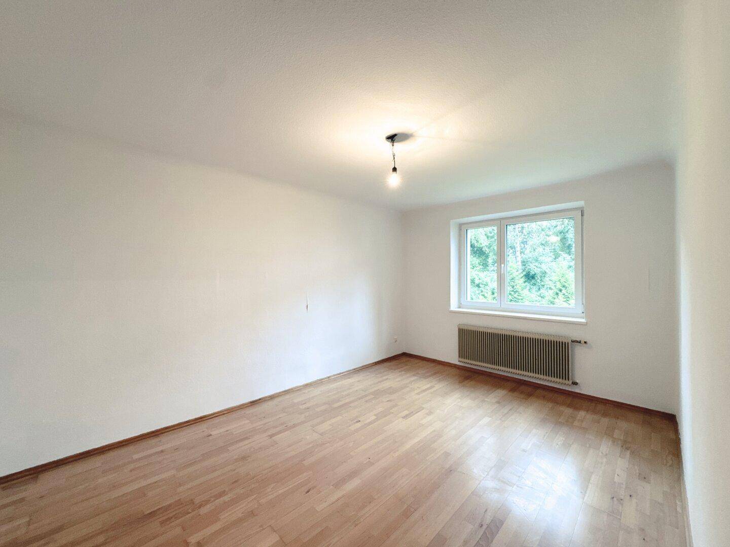 Helles, leeres Schlafzimmer mit Parkettboden und großem Fenster zum Garten.