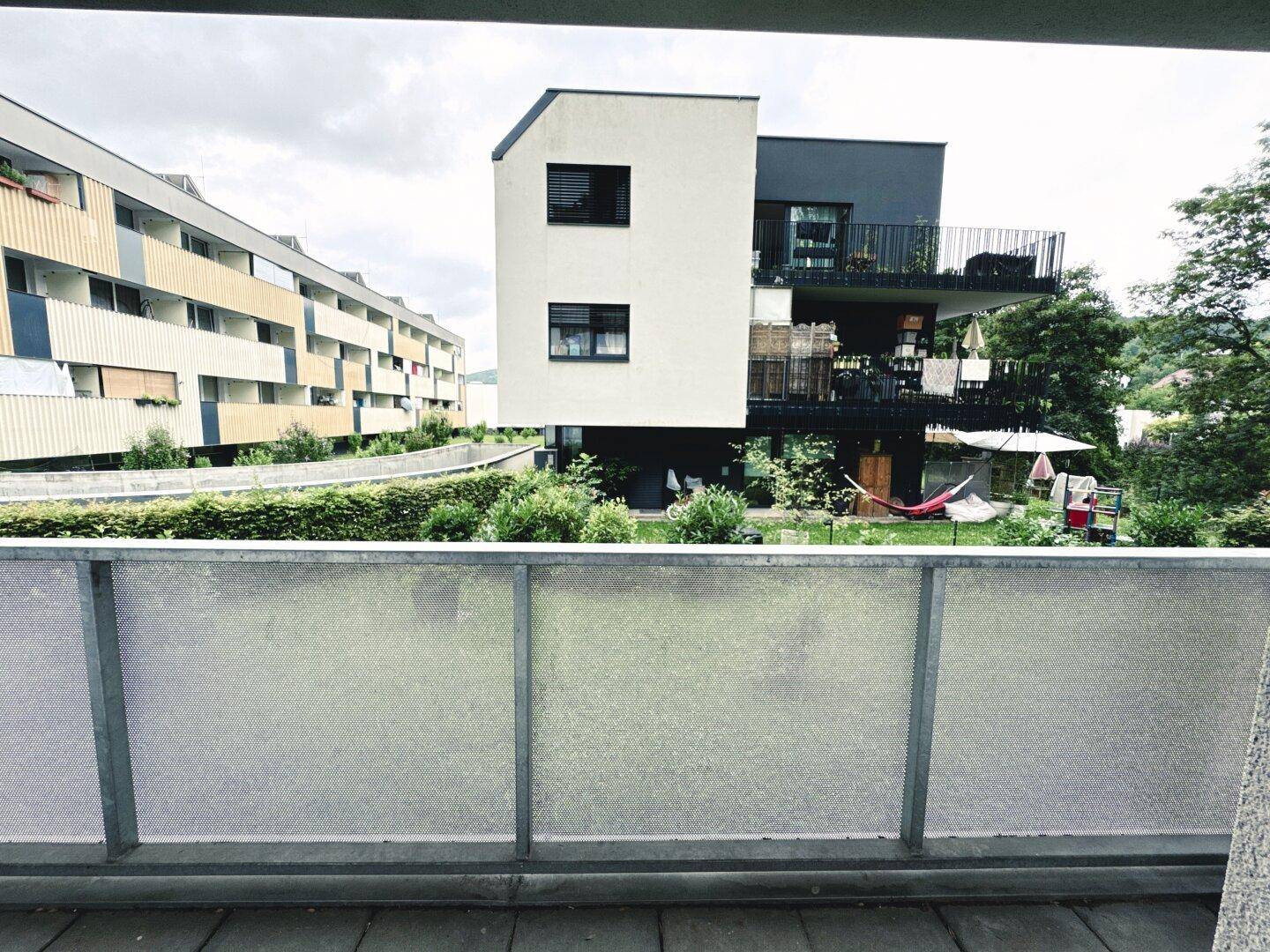Balkon mit Blick auf die umliegenden Wohngebäude und den grünen Gartenbereich.