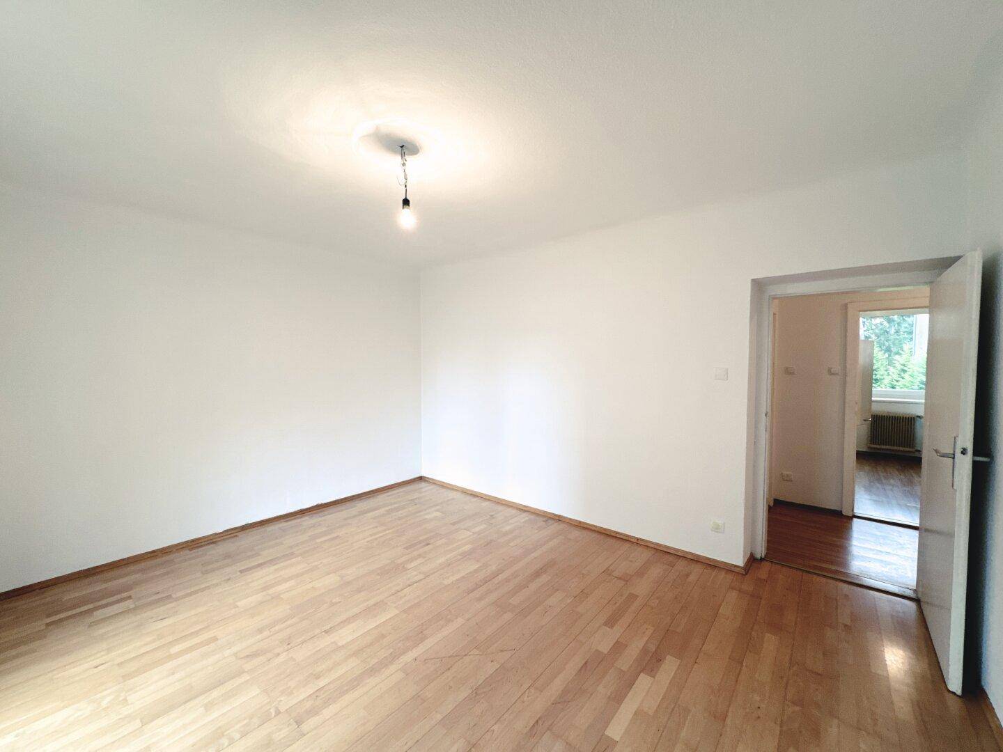 Geräumiges, leeres Zimmer mit Parkettboden und weiß gestrichenen Wänden.