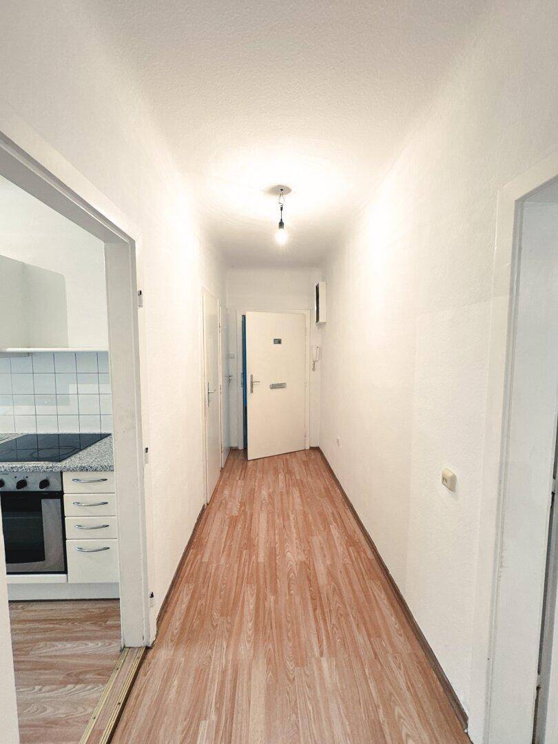 Heller Flur mit Laminatboden, der zur Eingangstür und Küche führt.