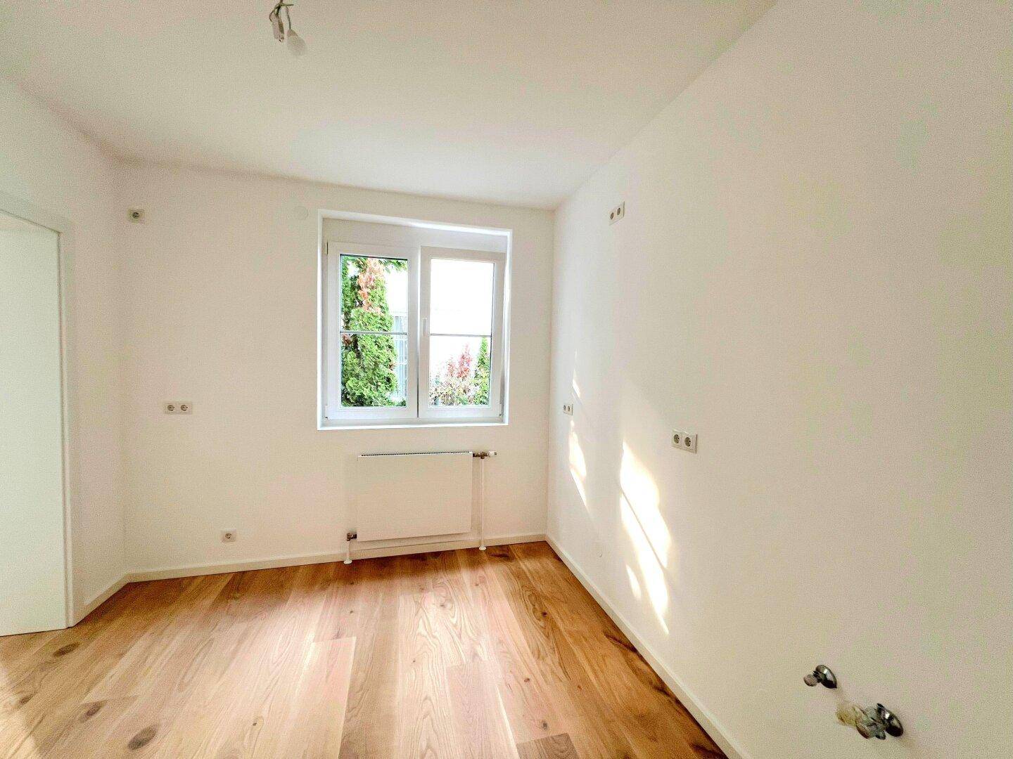 Helles Schlafzimmer mit Holzboden und einem Fenster, das Tageslicht hereinlässt.