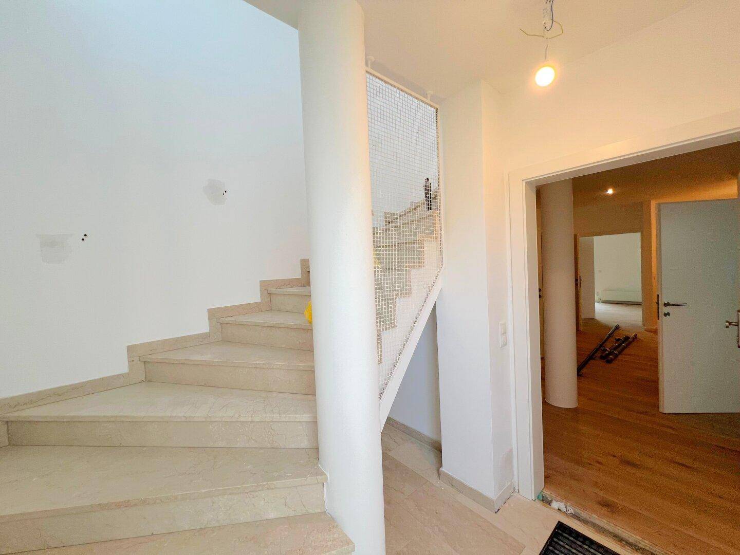 Elegante Treppe mit hellen Steinstufen und modernem Metallgeländer in einem hellen Eingangsbereich.
