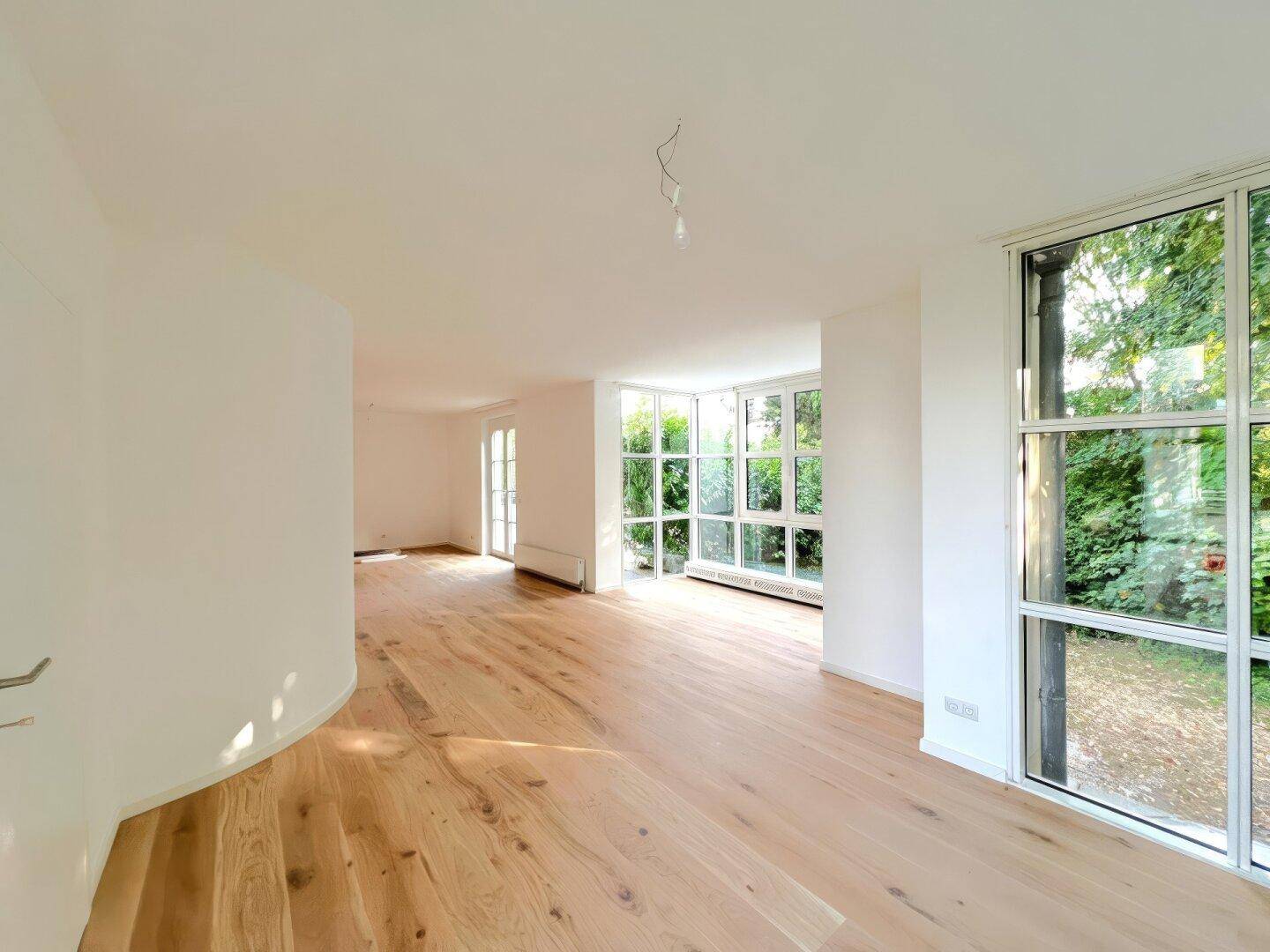 Helles Wohnzimmer mit Eichenparkett und großen Fenstern mit Blick ins Grüne.