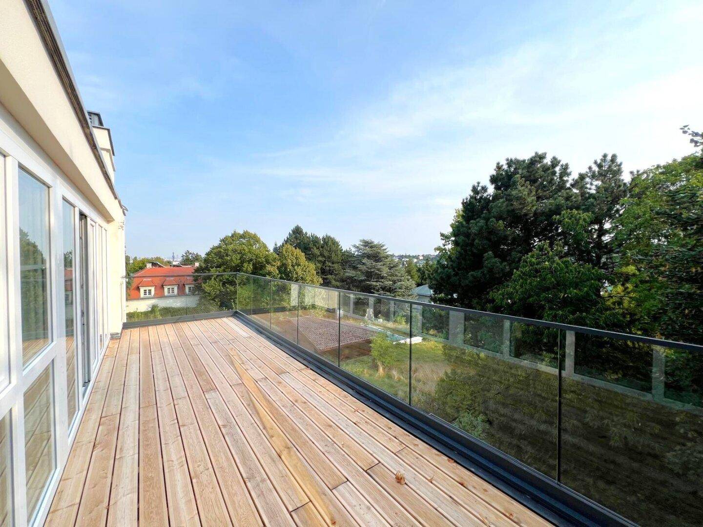Geräumige Holzterrasse mit Glasbrüstung und Panoramablick über die Baumwipfel.