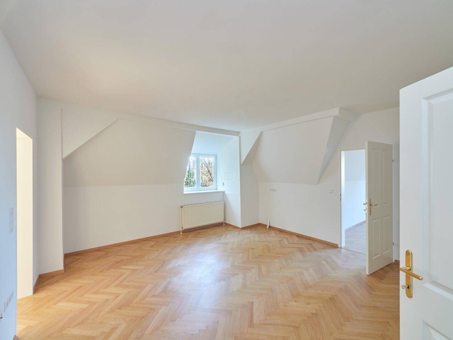Helles Zimmer im Dachgeschoss mit Fischgrätparkett, schrägen Wänden und natürlichem Lichteinfall.